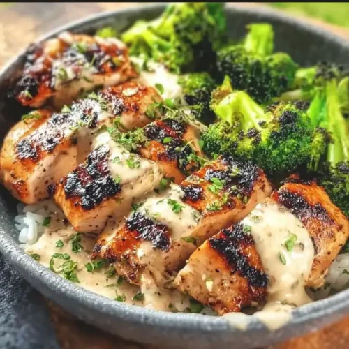 A top-down view of a Grilled Chicken and Broccoli Bowl with rice, showing the charred chicken, green broccoli, and a generous drizzle of creamy garlic sauce.