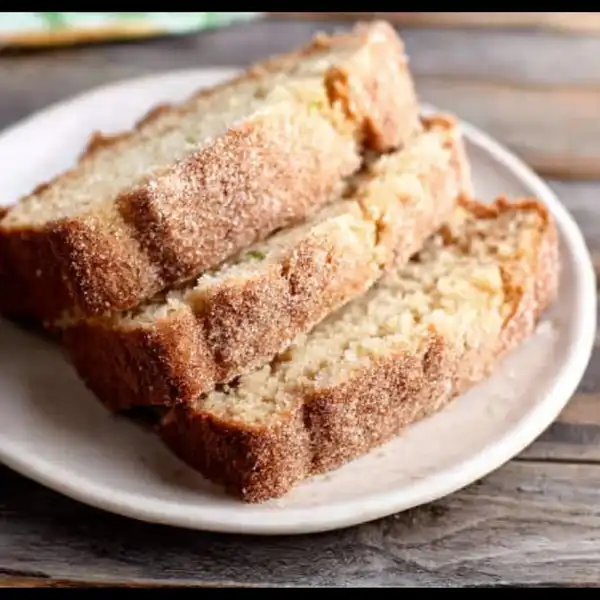 A whole loaf of golden-brown Snickerdoodle Zucchini Bread resting on a wire rack, featuring a deep, crackly cinnamon-sugar crust.