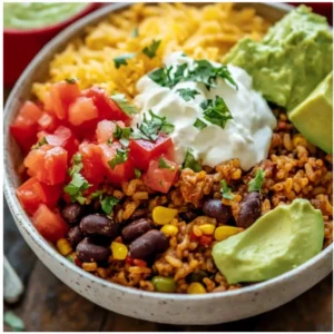 A close-up of a layered Taco Rice Bowl with a fork taking a bite, showing the seasoned beef, rice, beans, and fresh toppings.