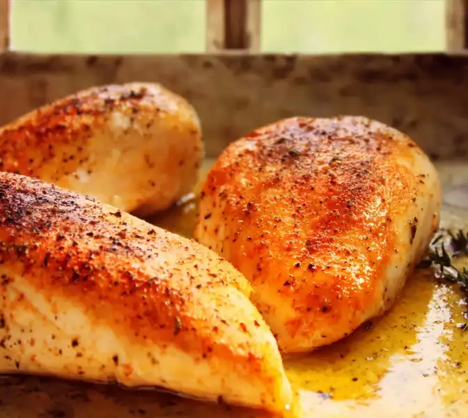 bake_chicken_brea_2_result Four golden-brown baked chicken breasts resting on a wooden cutting board, with one sliced to reveal a perfectly juicy and tender white interior.