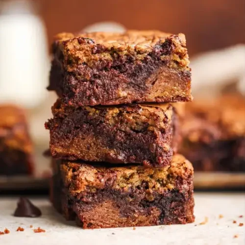 A perfect square of a brown butter brookies on parchment paper, showing the chewy cookie layer and the fudgy brownie layer.