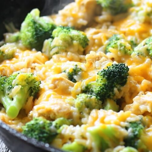 A large skillet of One-Pan Cheesy Chicken and Rice, with a golden blanket of melted cheddar cheese and vibrant green broccoli florets.