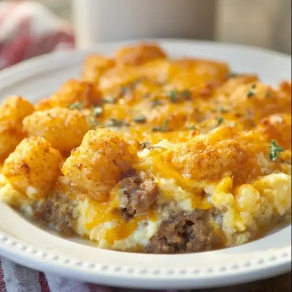 tater_tot_sausage_2_result A square slice of tater tot sausage casserole on a white plate, showing clean, distinct layers of egg, sausage, cheese, and a crispy top.