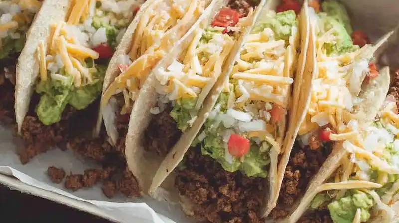 Juicy seasoned taco meat in warm tortillas garnished with tomatoes and cheese