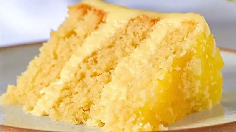 Pineapple cake slice on a white plate topped with whipped cream and pineapple filling