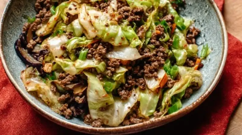 Chinese ground beef and cabbage stir fry served in a white bowl with scallions and rice.