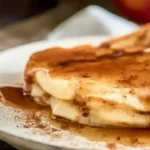Apple Pancakes with Cider Syrup dusted with powdered sugar in a cast iron skillet