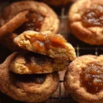 A stack of soft and chewy apple butter snickerdoodles cookies on a white plate, with one broken open to show the gooey apple butter center.