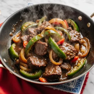 Easy Chinese pepper steak with tender beef and colorful bell peppers in a glossy sauce, sizzling in a wok.
