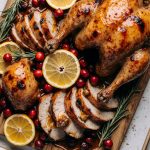 Ultimate cranberry orange glazed turkey resting on a platter with fresh rosemary and orange wedges.